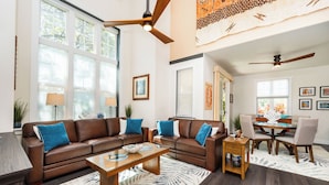 A spacious living room with a brown leather sectional sofa, a wooden coffee table, and a dining area with a glass table and chairs. - 💎Luxury Home Away From Home! 🏝Beach🌞Sunshine🏌️‍♂️Golfing  (Waikoloa)