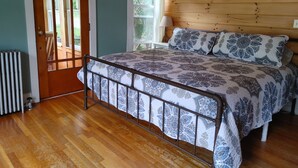 Quarto com estrutura de cama de madeira, colcha estampada e janela com vista para vegetação.