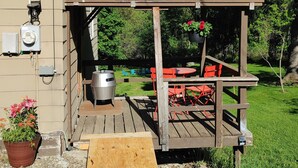 Um deck de madeira com pérgola, mobiliário para área externa e churrasqueira.