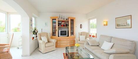 A spacious living room with a sofa, chairs, a glass coffee table, and a wooden cabinet.