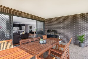 An outdoor dining area with a wooden table and chairs, a grill, and a brick wall. - Campanile House by Your Innkeeper Mudgee (Mudgee)