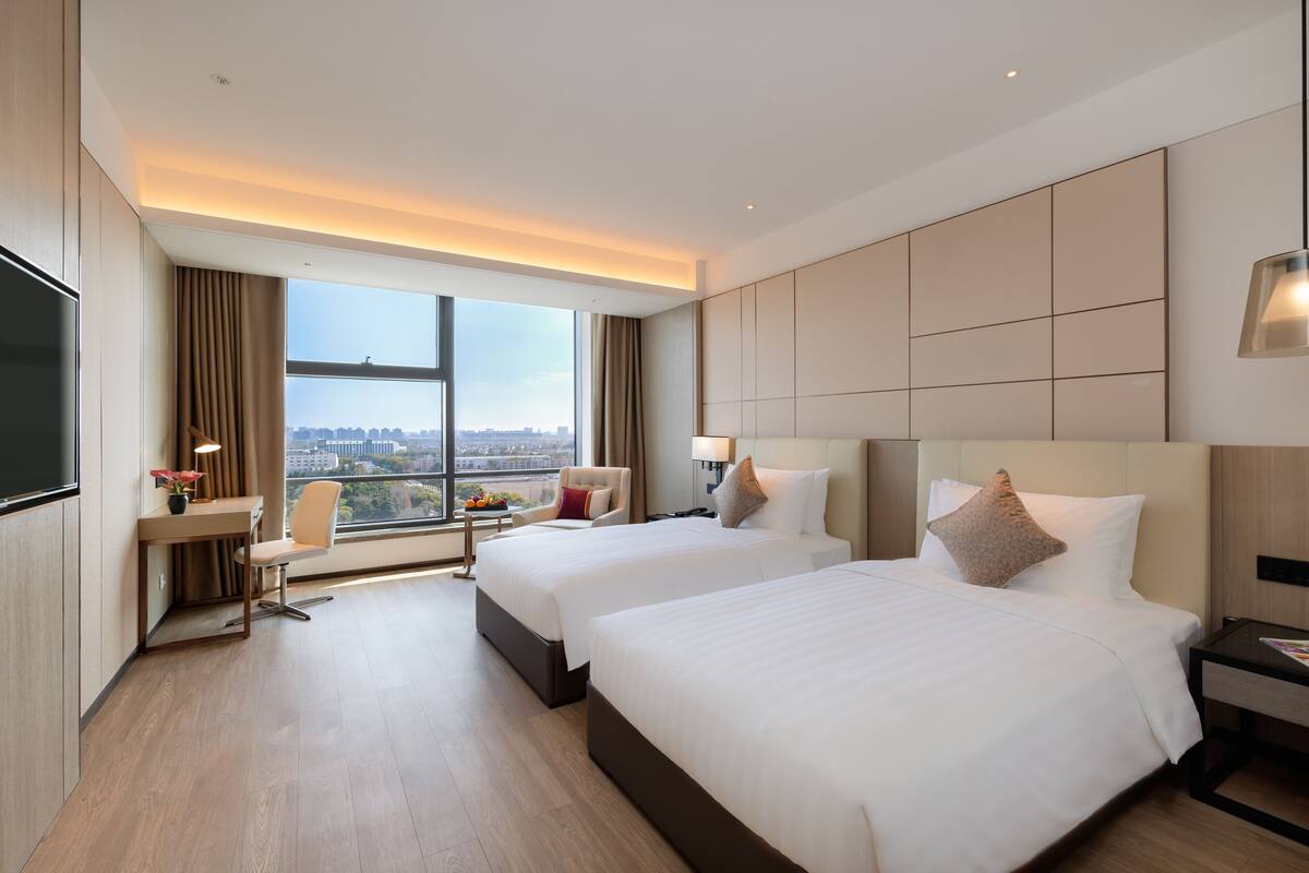 Une chambre d’hôtel avec deux lits, un bureau, une chaise et une grande fenêtre donnant sur la ville.