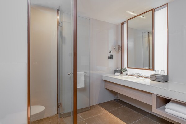 Un baño moderno con cabina de ducha de vidrio, un lavabo blanco con espejo y un mueble de tocador de madera.