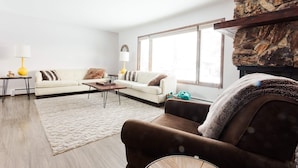 Ein modernes Wohnzimmer mit einem weißen Sofa, einem braunen Sessel, einem Couchtisch und einem Kamin mit einer Wand aus Naturstein.