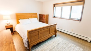 Ein Schlafzimmer mit einem hölzernen Bett, einem Nachttisch, einer Kommode und einem Fenster mit Jalousien.