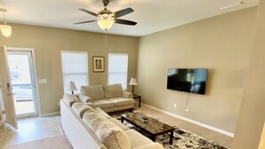 A living room with a sectional sofa, a coffee table, a TV mounted on the wall, and a ceiling fan. - Quiet and Beautiful House in a WONDERFUL location near 2 Lakes and Charlotte! (Huntersville)