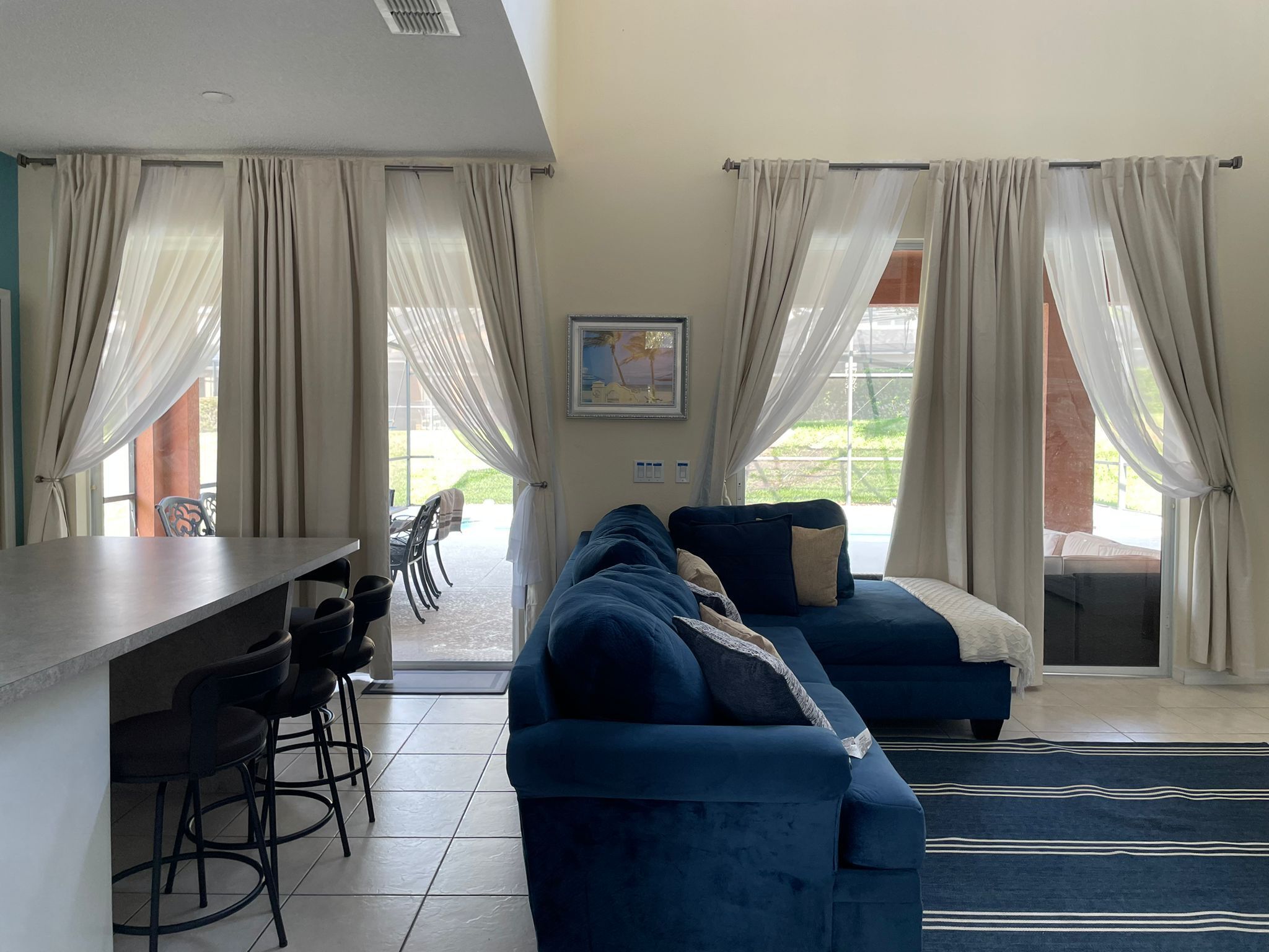 A modern living room with a sofa, a dining area with chairs, and large windows with curtains.
