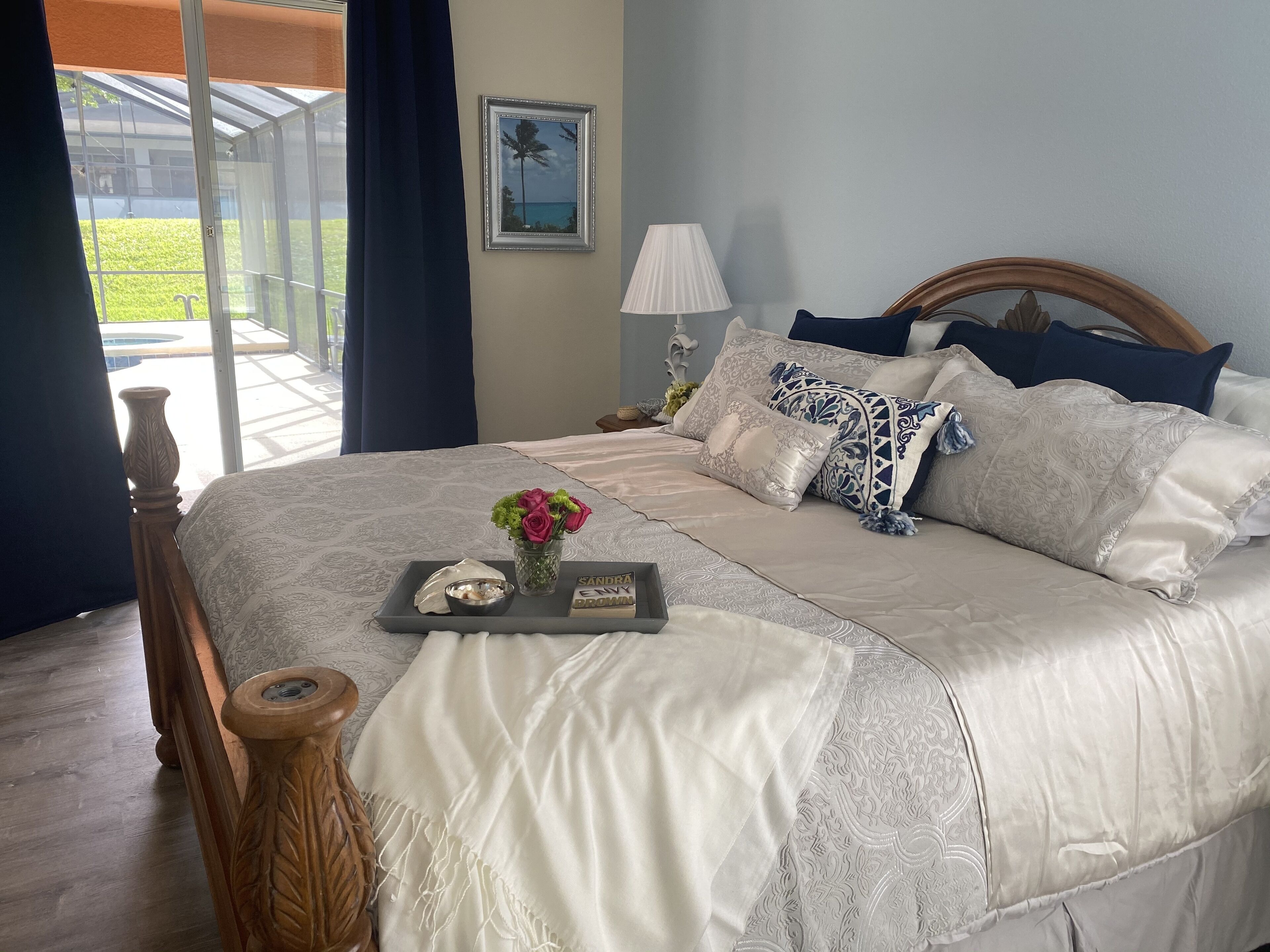 A neatly made bed with a tray of toiletries, a vase of flowers, and a framed picture on the wall.