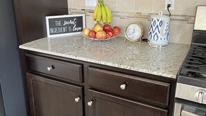 A kitchen with dark wooden cabinets, a granite countertop, a bowl of fruit, a kettle, and a sign that reads "The secret ingredient is love". - At last a new beautiful house is yours to enjoy (Clovis)