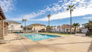 A swimming pool with lounge chairs, palm trees, and houses in the background. - At last a new beautiful house is yours to enjoy (Clovis)