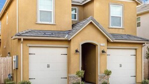 A two-story residential house with a beige exterior, two garage doors, and a small front entrance. - At last a new beautiful house is yours to enjoy (Clovis)