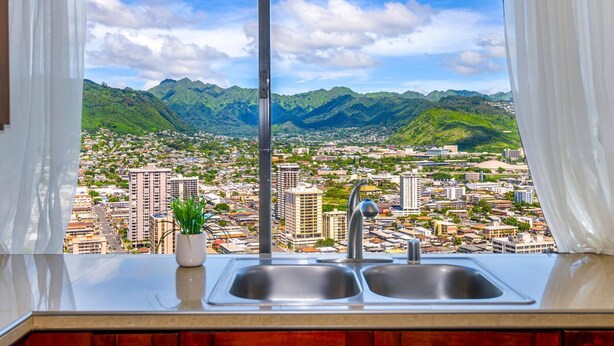 Una cocina con un lavamanos y vistas a un paisaje urbano y montañas.