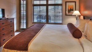 A hotel room with a bed, a dresser, a bench, a lamp, and a painting on the wall. - Grand Timber Lodge  Ski in/Ski out --two bedroom kitchenette (Breckenridge)