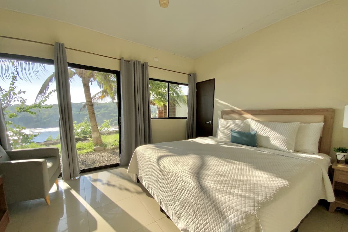 Un dormitorio con una cama grande, una silla y vistas al océano.