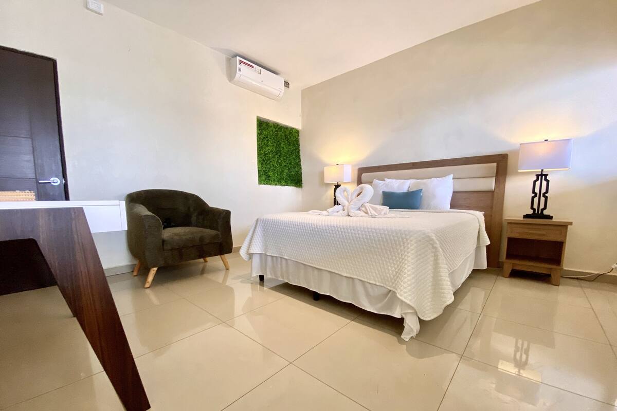 Habitación de hotel con cama, una silla, mesita de noche, aire acondicionado instalado en la pared y decoración verde en la pared.