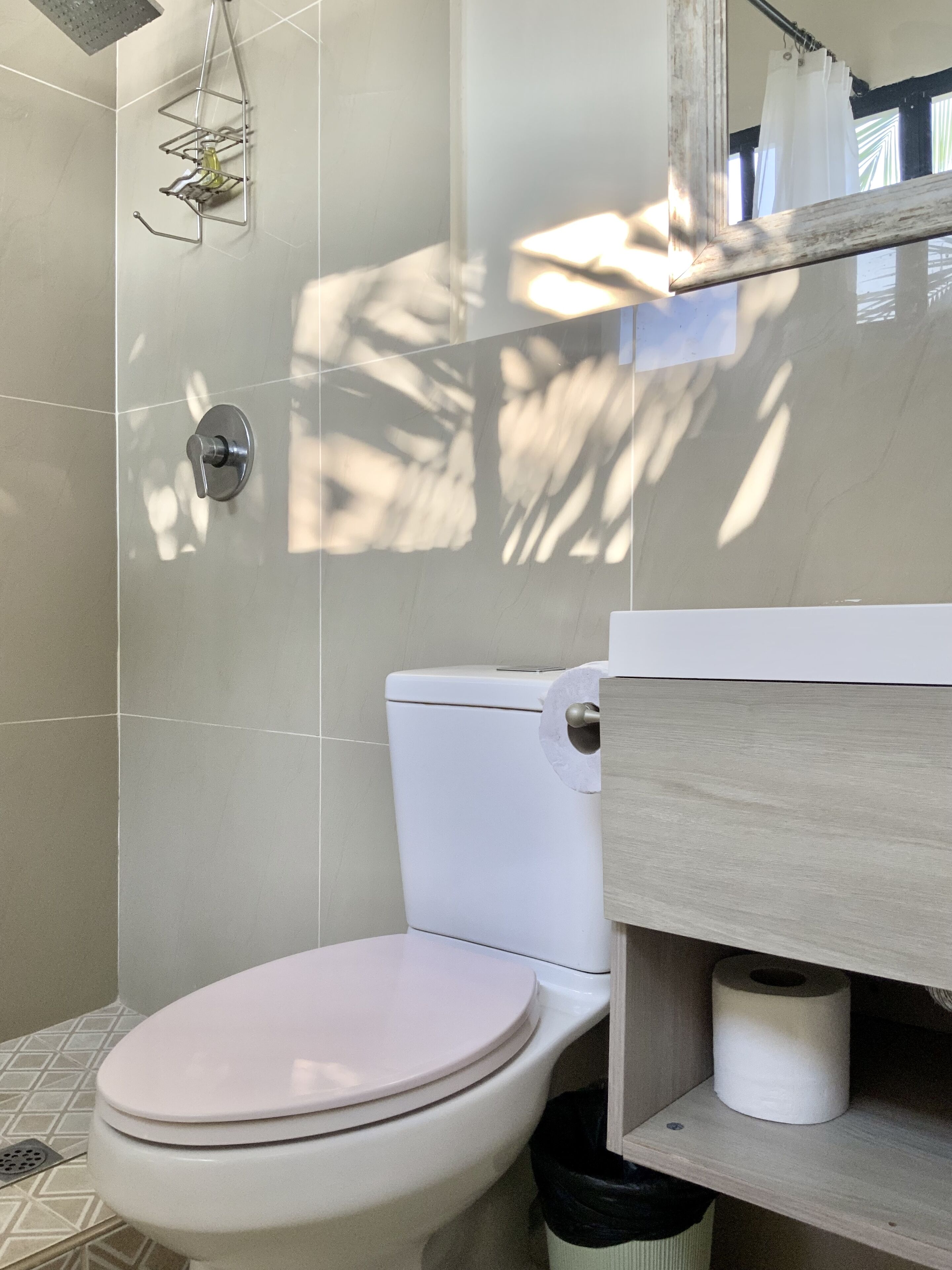 A bathroom with a toilet, a shower area, and a wooden vanity with a toilet paper holder.