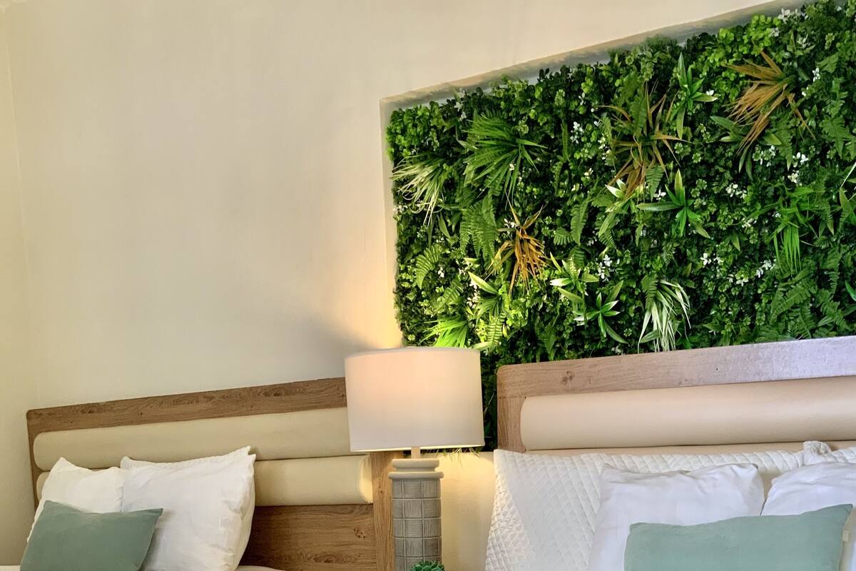 Habitación de hotel con dos camas, cabecero de madera, pared verde decorativa y lámpara de noche.
