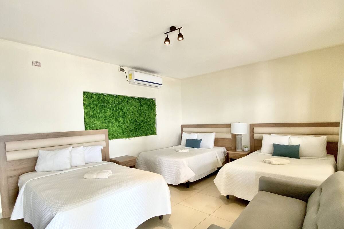 Habitación de hotel con tres camas, un sofá, una pared verde y una lámpara en el techo.