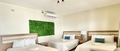 A hotel room with three beds, a sofa, a green wall, and a ceiling light fixture.