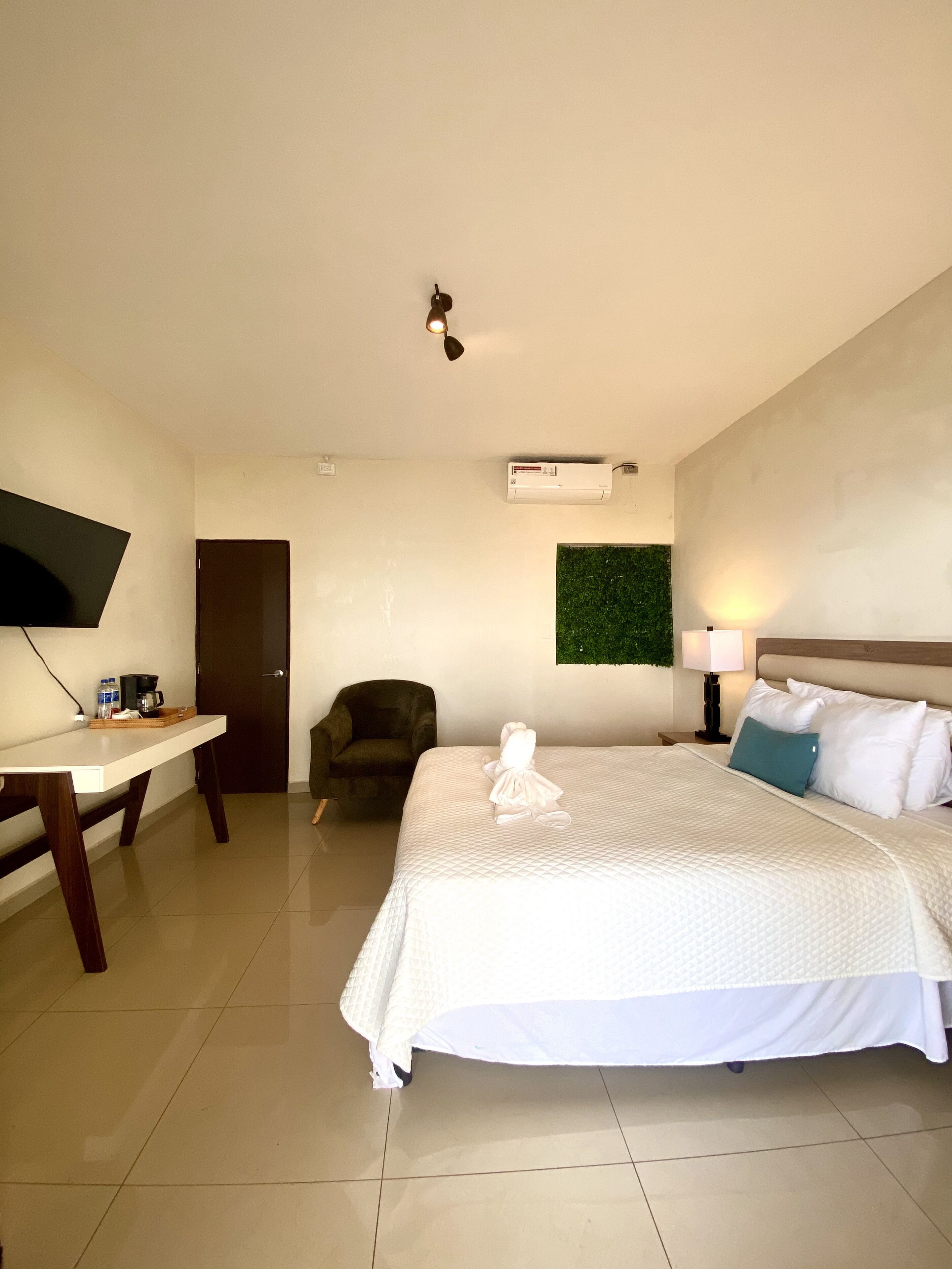 A hotel room with a bed, a desk, a chair, a TV, and a wall-mounted air conditioner.