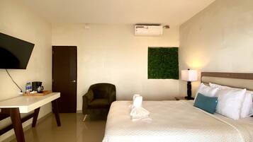 A hotel room with a bed, a desk, a chair, a TV, and a wall-mounted air conditioner.