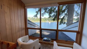 Une pièce dotée d’une grande fenêtre donnant sur un lac, de deux fauteuils rembourrés et d’une petite table ronde.