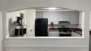 Una cucina compatta con mobili bianchi, un frigorifero nero, un fornello e una macchina per il caffè.