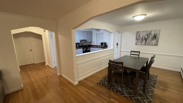 Un'ampia sala da pranzo con tavolo e sedie in legno, una cucina sullo sfondo e un corridoio che conduce a una porta.