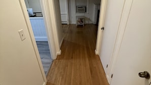 Un corridoio con pavimento in legno, pareti bianche e una porta a destra.