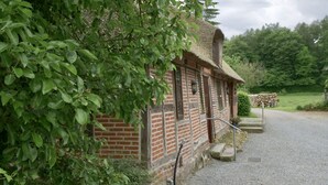 A rustic brick building with a thatched roof, surrounded by lush greenery and a gravel path leading to it. - Reetdachkate im Herzen Angelns (Schnarup-Thumby)
