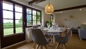 A dining area with a table set for four, large windows, and a hanging light fixture. - Reetdachkate im Herzen Angelns (Schnarup-Thumby)