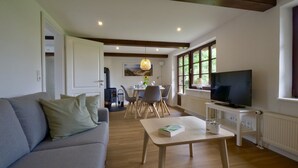 A living room with a sofa, a dining table with chairs, a TV, and a fireplace. - Reetdachkate im Herzen Angelns (Schnarup-Thumby)