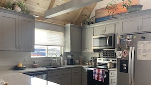 A kitchen with grey cabinets, a stainless steel refrigerator, a microwave, and a stove. - ReTreat yourself with this sunny A-frame experience (delta)