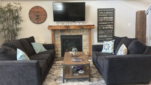 A cozy living room with two dark sofas, a wooden coffee table, a stone fireplace, a clock, and a motivational quote wall. - ReTreat yourself with this sunny A-frame experience (delta)