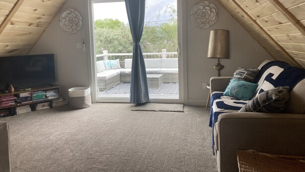 A cozy attic bedroom with a sloped ceiling, a large window with curtains, a TV, a sofa with cushions, and a lamp. - ReTreat yourself with this sunny A-frame experience (delta)