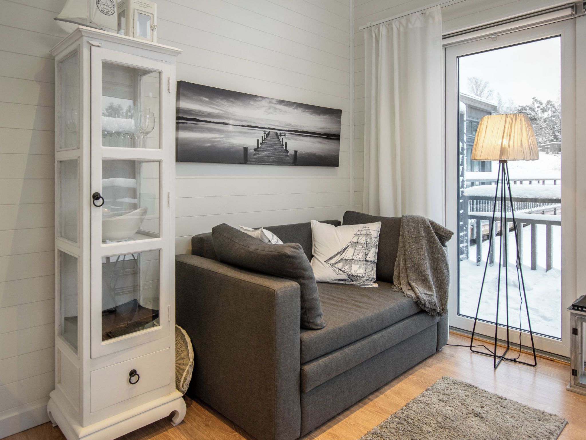 A modern living room with a grey sofa, a white cabinet, and a large window with a view of a snowy landscape.