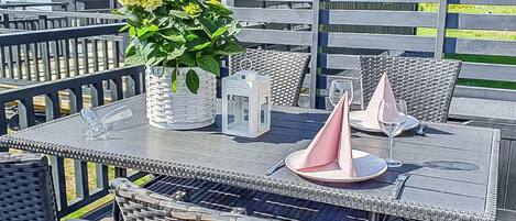 An outdoor dining area with wicker furniture, a table set with plates, glasses, and a potted plant.