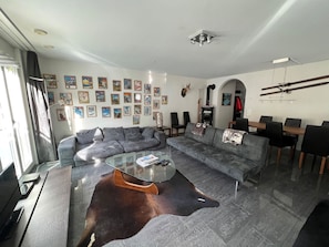 Una sala moderna con un sofá modular, una mesa de centro de vidrio, un tapete de cuero y una zona de comedor con sillas.