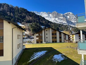 A residential area with modern buildings, a grassy courtyard, and a mountain backdrop.