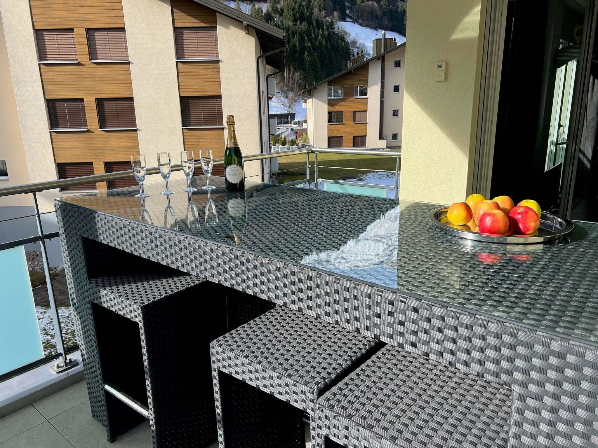 A glass-top outdoor bar with seating, a bottle of champagne, and a fruit bowl.