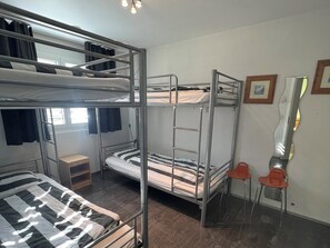 A bunk bed room with a small wooden nightstand and a red chair.