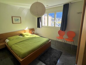 Un dormitorio con cama, lámparas de noche, una ventana con cortinas y vistas al exterior, además de dos sillones.
