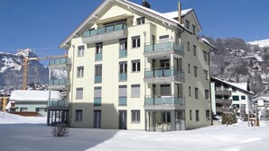Monikerroksinen hotelli, jossa on parvekkeet, savupiippu ja lumihuippuisten vuorten muodostama tausta.