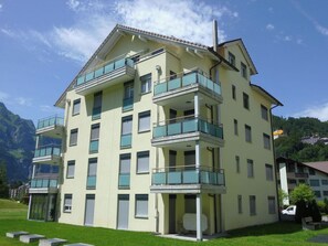 Un edificio de varios pisos con balcones, una chimenea y montañas al fondo.