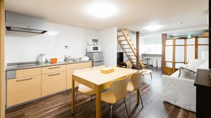 Eine kompakte Küche mit modernen Geräten, ein Essbereich mit Holztisch und -stühlen sowie eine Treppe, die in eine weitere Ebene führt.