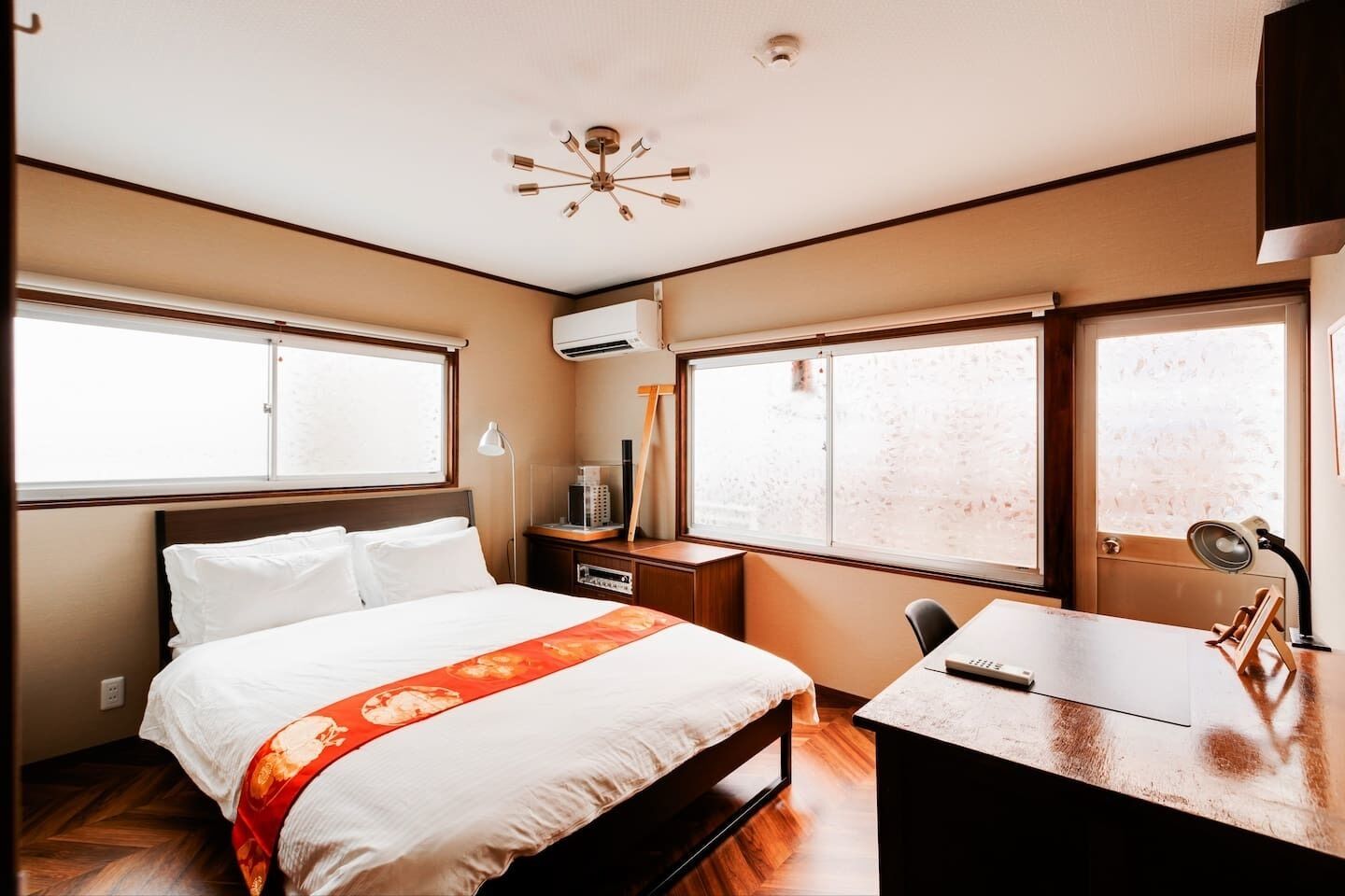 A hotel room with a bed, desk, and two windows.