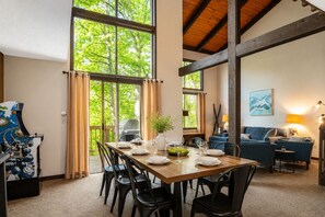 Un coin repas avec une table en bois dressée pour quatre personnes, entourée de chaises noires, et offrant une vue sur la verdure à l’extérieur.