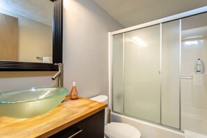 A bathroom with a glass bowl sink, a wooden countertop, a white toilet, and a frosted glass shower enclosure.