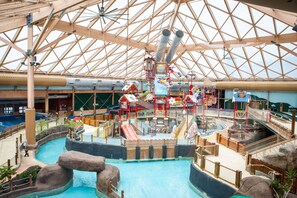 Een overdekt waterpark met een groot zwembad, glijbanen en speelconstructies.