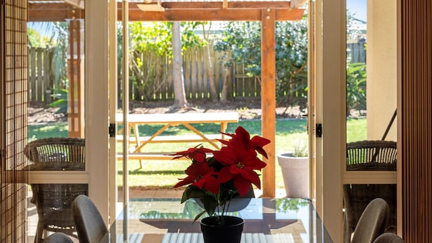 Une porte vitrée donne sur un patio extérieur agrémenté d’une pergola en bois, d’une table et de chaises.